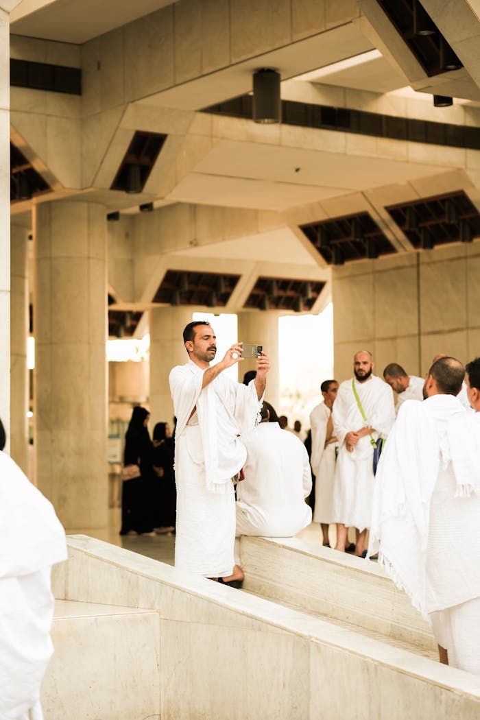 Pilgrims dressed in traditional attire capture moments at a religious site in Saudi Arabia.