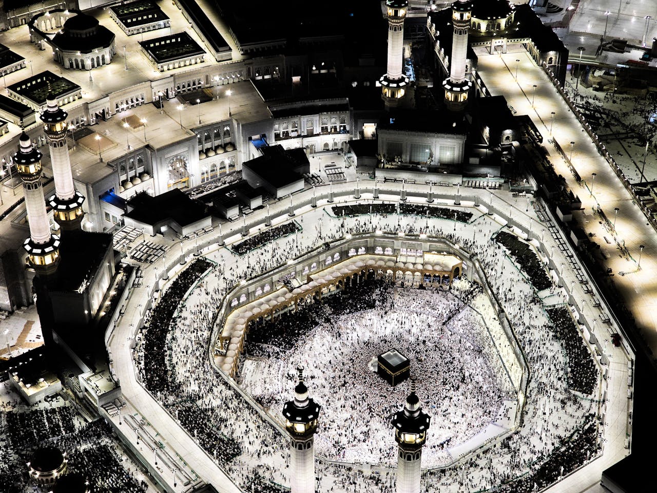 gallery-4 Stunning aerial photograph of the Grand Mosque in Mecca, illuminated at night, showcasing the Kaaba and worshippers.